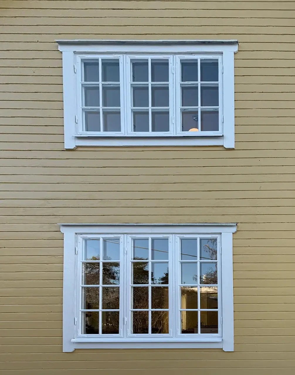 Två vita fönster med spröjs på en beige trävägg.